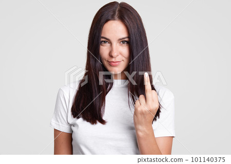 Bad girl with straight dark hair shows fuck sign, looks mysteriously at camera, wears casual t shirt, isolated over white background. Young brunette young woman shows middle finger. Fuck off! Bad girl with straight dark hair shows fuck sign, looks mysteriously at camera, wears casual t shirt, isolated over white background. Young brunette young woman shows middle finger. Fuck off! 101140375