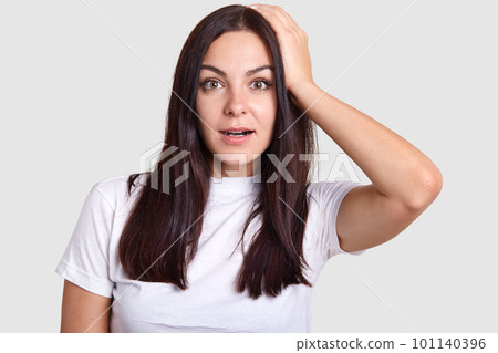 Pretty brunette female with wide open mouth in portrait photo poses for photographer who asks to show different situations. Model stands on isolated gray background and looks into center of lens. 101140396