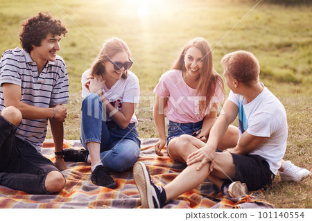Friends, happiness and leisure concept. Photo of friendly teenagers meet together on nature, have picnic, tell each other funny stories, enjoy summer weather and sunshine, have positive smiles 101140554