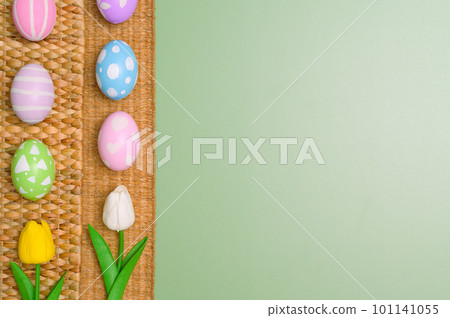 Happy Easter holiday greeting card design concept. Colorful Easter Eggs and spring flowers on pastel green background. Flat lay, top view, copy space. 101141055