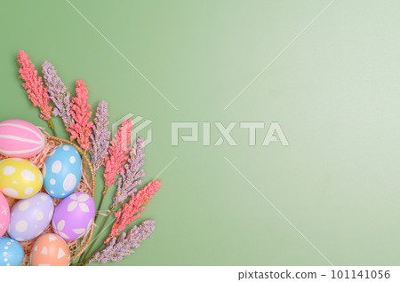 Happy Easter holiday greeting card design concept. Colorful Easter Eggs and spring flowers on pastel green background. Flat lay, top view, copy space. 101141056