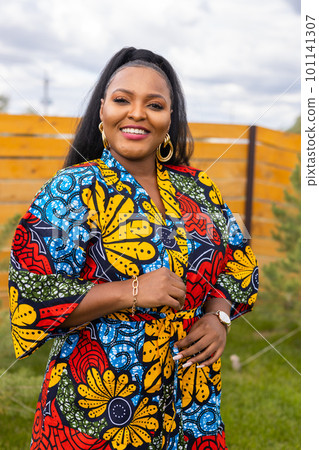 Summer portrait of beautiful african american woman in colourful dress wear standing on backyard. Suburban lifestyle and chilling on weekend in countryside and inclusion with diversity concept Summer portrait of beautiful african american woman in colourful dress wear standing on backyard. Suburban lifestyle and chilling on weekend in countryside and inclusion with diversity concept 101141307
