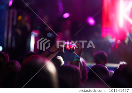 Hand with a phone records live music festival. People taking photographs with smart phone during concert. 101141437