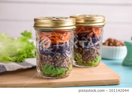 Glass jars with healthy meal on light blue wooden table Glass jars with healthy meal on light blue wooden table 101142044