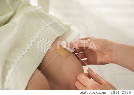 Mother putting sticking plaster onto daughter's leg indoors, closeup Mother putting sticking plaster onto daughter's leg indoors, closeup 101142159