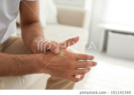 Man putting sticking plaster onto hand indoors, closeup Man putting sticking plaster onto hand indoors, closeup 101142160