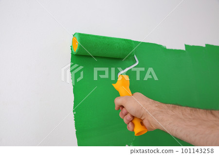 Man painting white wall with green dye, closeup. Interior renovation 101143258