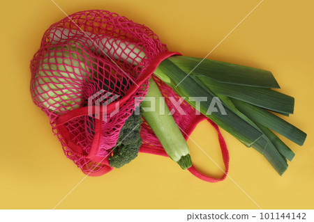 Net bag with vegetables on yellow background, top view 101144142