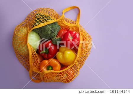 Net bag with vegetables on lilac background, top view Net bag with vegetables on lilac background, top view 101144144