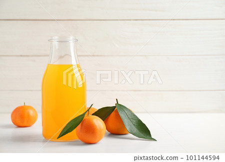 Fresh tangerines and bottle of juice on white wooden table. Space for text 101144594