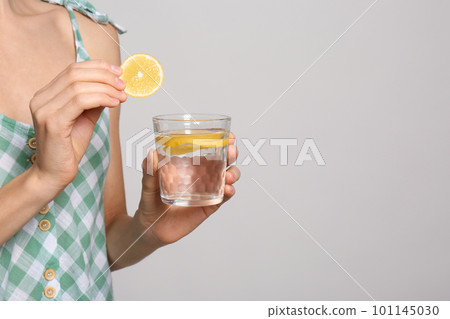 Young woman with glass of lemon water on light background, closeup. Space for text Young woman with glass of lemon water on light background, closeup. Space for text 101145030