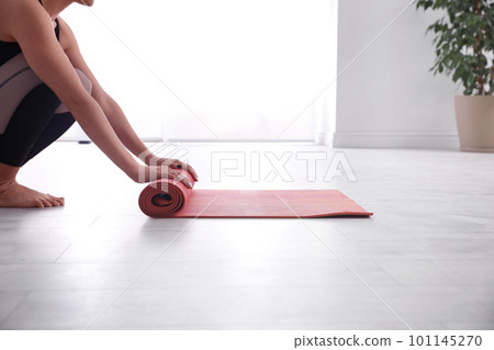 Woman rolling her mat on floor in yoga studio, closeup Woman rolling her mat on floor in yoga studio, closeup 101145270