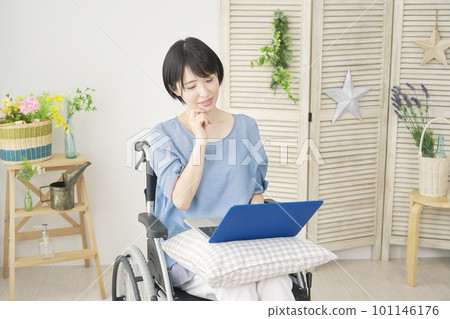 Woman in a wheelchair using a laptop in the living room Woman in a wheelchair using a laptop in the living room 101146176
