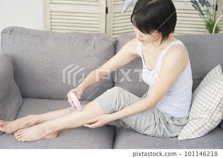 A woman doing self hair removal on her legs with a home epilator in the living room A woman doing self hair removal on her legs with a home epilator in the living room 101146218