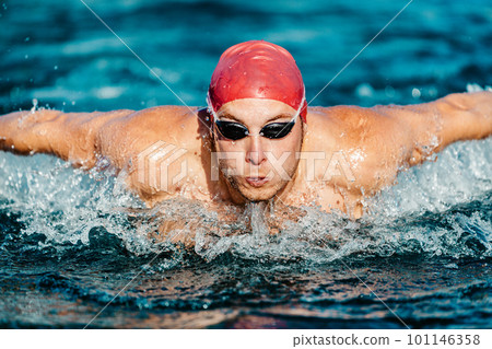 Swimming man. Male Swimmer athlete doing butterfly swim stroke. Male sport fitness man wearing swimming goggles and swim cap training hard in outdoor pool. Professional sports fitness model 101146358
