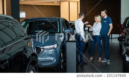 The seller hands over the car keys to the buyers. The couple bought a new car. The seller hands over the car keys to the buyers. The couple bought a new car. 101147600