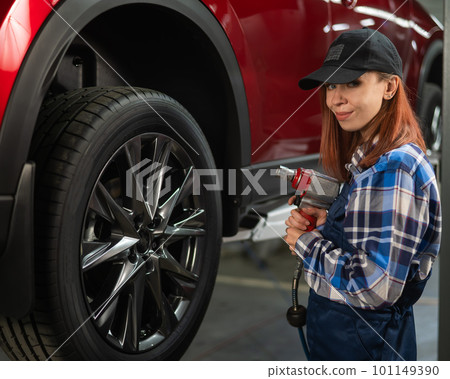 Woman mechanic uses pneumatic wrench to tighten the wheel nut. Girl at men's work.  101149390