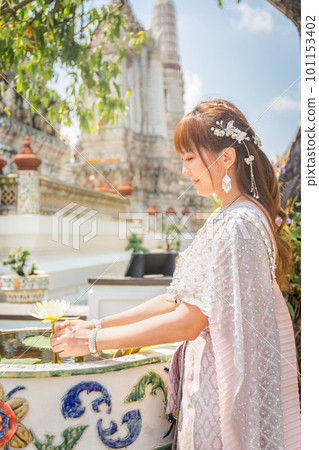 Young woman wearing traditional Thai dress with accessories stands holding a lotus flower at Wat Arun, a popular destination for tourists around the world. Bangkok Thailand Young woman wearing traditional Thai dress with accessories stands holding a lotus flower at Wat Arun, a popular destination for tourists around the world. Bangkok Thailand 101153402