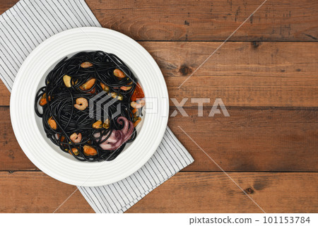 Black seafood pasta in white plate over linen towel on rustic background . Black Mediterranean spaghetti on wood background with copy space. Black seafood pasta in white plate over linen towel on rustic background . Black Mediterranean spaghetti on wood background with copy space. 101153784