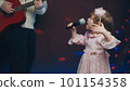 Little girl on stage in vintage dress, she sings into microphone and dances, her father plays acoustic guitar. Color music is shining and smoke is billowing. Father and Child Day, performance on stage 101154358