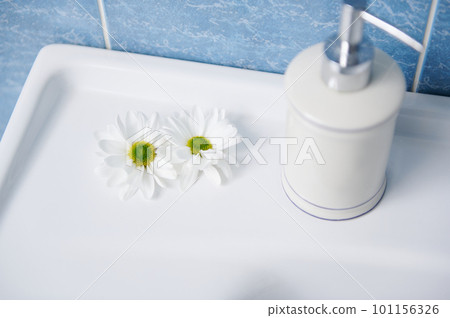 Stylish white ceramic dispenser with antiseptic antibacterial liquid soap and chamomile flowers on a white wash basin in the home bathroom. View from above. Still life 101156326