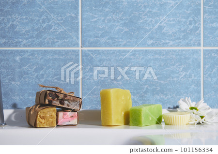 Still life with organic cold pressed soap bars with herbal ingredients and essential oils, for purity, home spa, skin and body care, on the bathroom wash basin against blue marble wall background 101156334