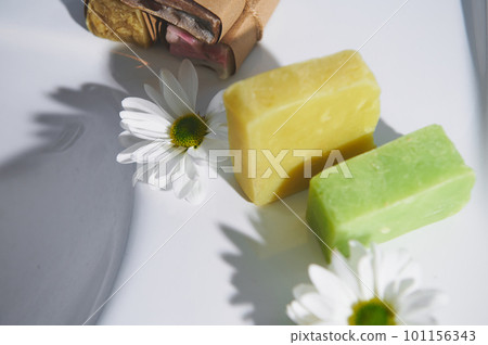 Handmade organic eco soap with natural ingredients of olive oil and chamomile on white ceramic washbasin. Natural ecologically friendly cosmetic products for home spa, skin and body care. Top view Handmade organic eco soap with natural ingredients of olive oil and chamomile on white ceramic washbasin. Natural ecologically friendly cosmetic products for home spa, skin and body care. Top view 101156343