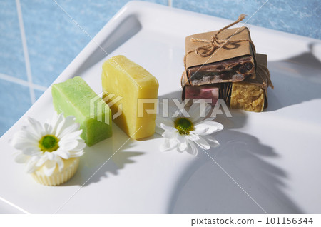 Still life with various handmade eco soap bars and solid shampoo with natural ingredients of lavender, coffee beans, olive oil, essential oils and chamomile, on a white ceramic surface in the bathroom 101156344