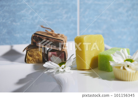 Still life. Assortment of craft organic soap bars with herbal ingredients and essential oils, for purity, home spa, skin and body care, on the bathroom wash basin against blue marble wall background 101156345