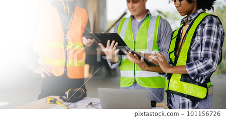 colleagues discussing data working and tablet, laptop with on on architectural project at construction site at desk in office. 101156726