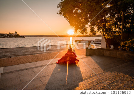 Sunrise red dress. A woman in a long red dress against the backdrop of sunrise, bright golden light of the sun's rays. The concept of femininity, harmony. 101156953