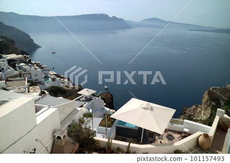 A row of white houses built on volcanic rocks on a cliff and the Aegean Sea 101157493