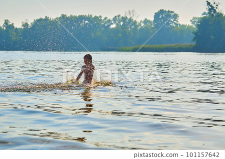 Pleased happy child bathes plays with splashes in a warm summer river, lake 101157642