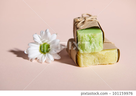 Still life with handmade organic cold pressed soap bars with natural ingredients and chamomile flower, wrapped in eco craft paper, on isolated pink background. Hygiene. Skin and body care concept Still life with handmade organic cold pressed soap bars with natural ingredients and chamomile flower, wrapped in eco craft paper, on isolated pink background. Hygiene. Skin and body care concept 101159976