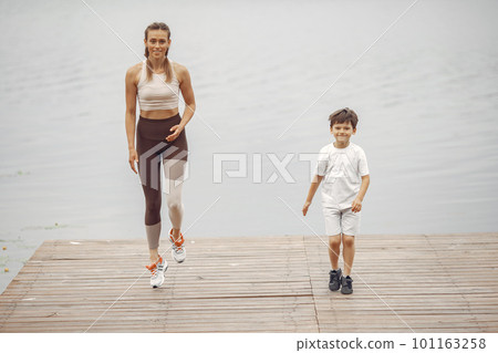 Son and mother are doing exercises in the summer park. Family by the water. 101163258