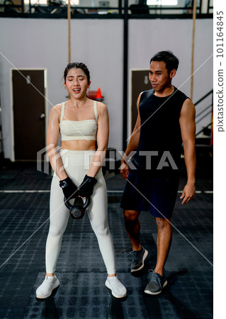 Asian sport woman hold weight to exercise with support by the trainer in fitness gym. 101164845