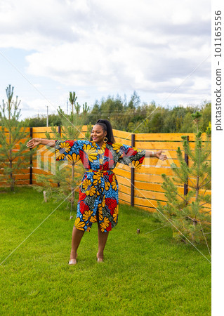 Summer portrait of beautiful african american woman in colourful dress wear standing on backyard. Suburban lifestyle and chilling on weekend in countryside and inclusion with diversity concept Summer portrait of beautiful african american woman in colourful dress wear standing on backyard. Suburban lifestyle and chilling on weekend in countryside and inclusion with diversity concept 101165556