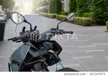 Electric scooter with connected charging cable on a city street Electric scooter with connected charging cable on a city street 101167073