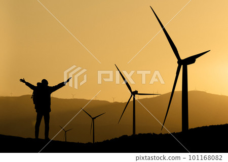 Silhouettes of a traveler and wind turbines at sunset 101168082
