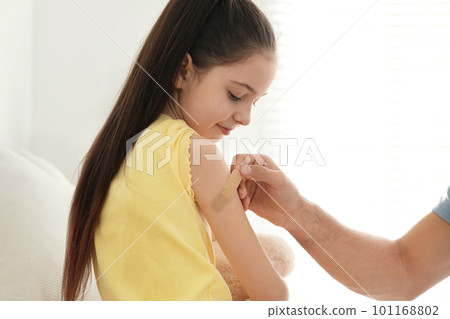 Father putting sticking plaster onto daughter's arm at home 101168802