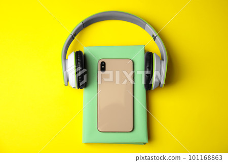 Book with mobile phone and headphones on yellow background, flat lay 101168863