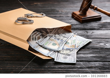 Envelope with dollar bills and handcuffs on black wooden table. Bribe concept 101168883