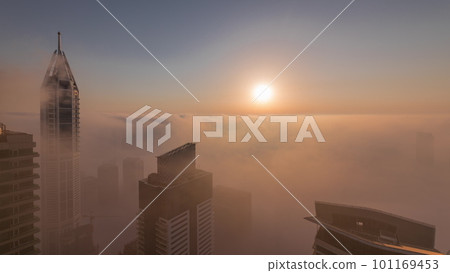 Rare early morning winter fog above the Dubai Marina skyline and skyscrapers lighted by sun aerial timelapse. 101169453