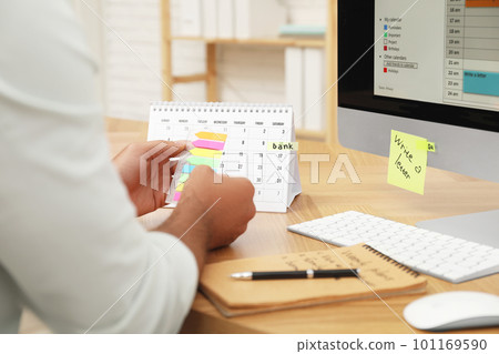 Man putting sticker on calendar at table in office, closeup 101169590
