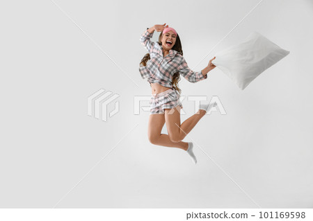 Beautiful woman with pillow jumping on light grey background. Bedtime Beautiful woman with pillow jumping on light grey background. Bedtime 101169598