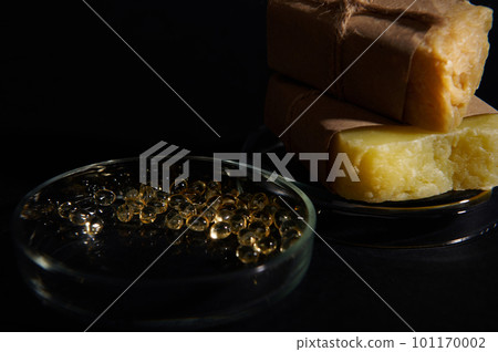 Selective focus on golden color translucent gel capules with essential acids and oils in laboratory Petri dish, on the background of homemade natural organic soap bars, isolated over black background Selective focus on golden color translucent gel capules with essential acids and oils in laboratory Petri dish, on the background of homemade natural organic soap bars, isolated over black background 101170002