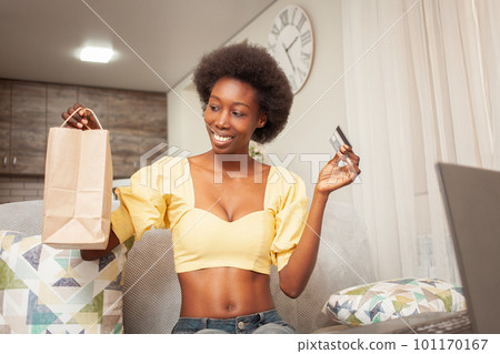 African American black woman at home sitting in front of laptop, online shopping, home delivery, bank card. Discounts promotions in the store. holiday gift 101170167
