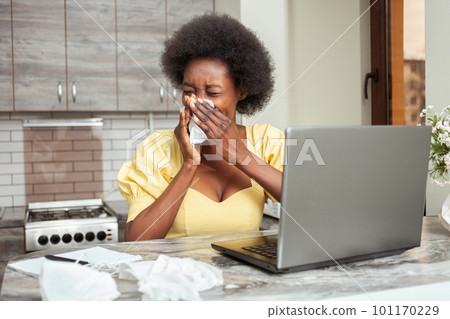 sick African American woman sneezes coughing. Freelancer, home office, work on laptop. Unhealthy sick African American woman sneezes coughing. Freelancer, home office, work on laptop. Unhealthy 101170229