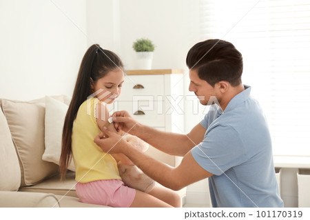 Father putting sticking plaster onto daughter's arm at home 101170319