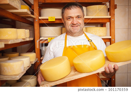 Cheese seller in store, home production, business, entrepreneur. Smiling man, portrait. Businessman, sale of cheese products. Made with love and care. holds in his hands 101170359